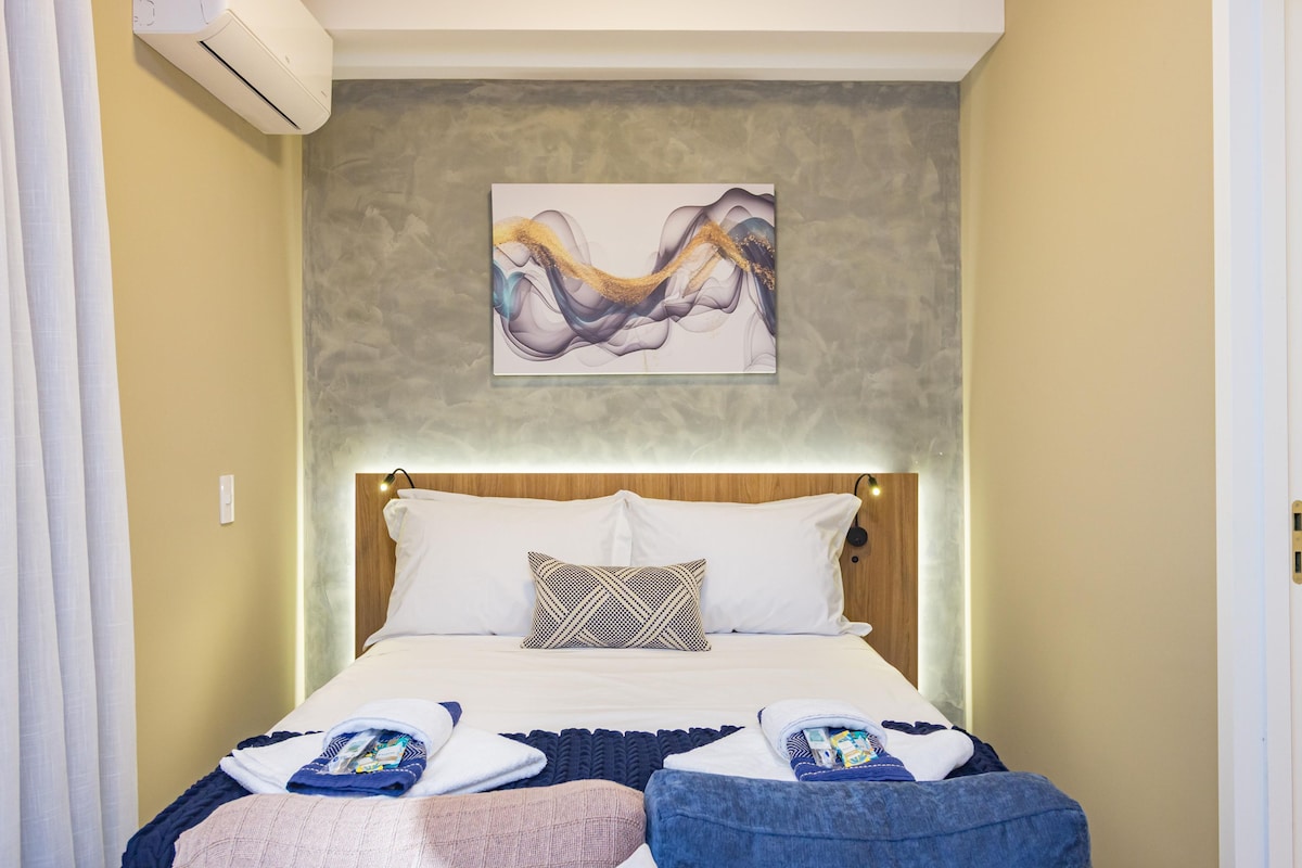 A hotel room with a bed, pillows, a blanket, and a wall-mounted artwork.