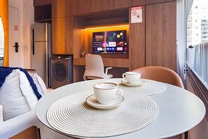 Ett modernt hotellrum med ett runt matbord, två vita koppar med tillhörande fat, en tv som är monterad på väggen och utsikt över staden genom fönstret.