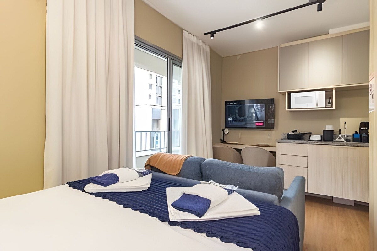 A hotel room with a bed, a desk, a television, and a view of the outside.