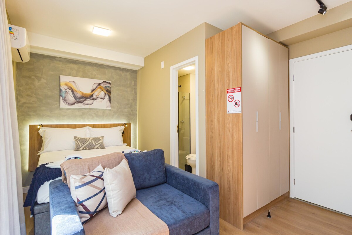 A hotel room with a bed, a blue sofa, a wooden wardrobe, a white door, and a shower area.