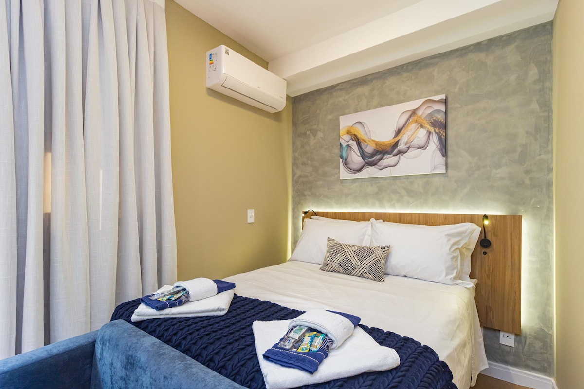 A hotel room with a bed, a wall-mounted air conditioner, and a painting.