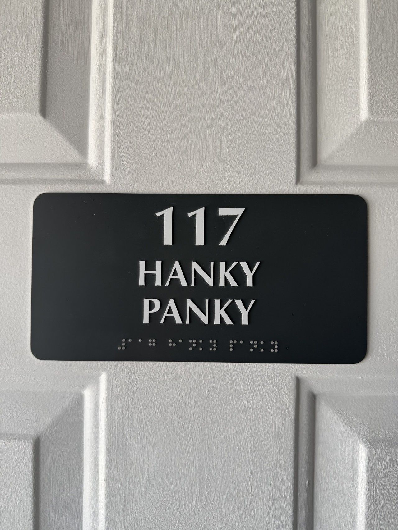 Un cartel con el número 117 y el nombre 'HANKY PANKY' en una puerta blanca.