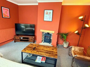 A living room with a television, a fireplace, a coffee table, and a chair. - Artistic house in Peaceful Kingswood (South Gloucestershire)