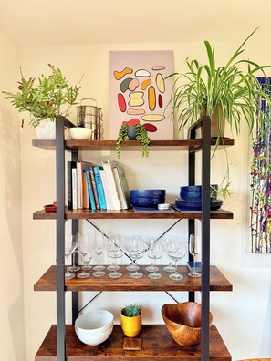 A multi-tiered wooden shelf with plants, books, and glassware. - Artistic house in Peaceful Kingswood (South Gloucestershire)