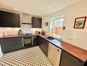 A modern kitchen with dark cabinets, a patterned floor, and a window with a view. - Artistic house in Peaceful Kingswood (South Gloucestershire)