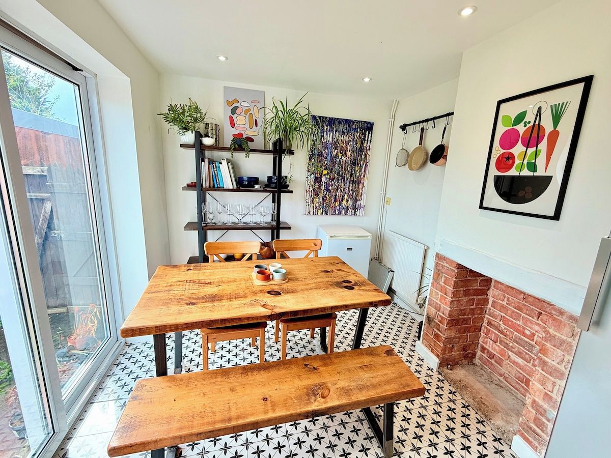 A dining area with a wooden table and benches, a brick fireplace, and a view through a sliding glass door.