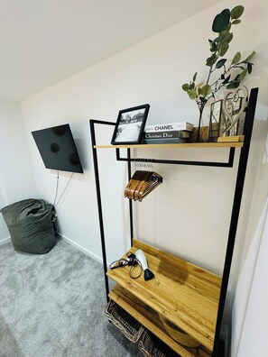 A room with a black TV mounted on the wall, a wooden shelf with books and a plant, a grey bean bag chair, and a small wooden table with a lamp and a phone. - Exquisite Apartment in City Centre (Redcliffe)