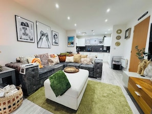 A modern living room with a sectional sofa, a green rug, and a kitchen in the background. - Exquisite Apartment in City Centre (Redcliffe)