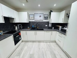 A modern kitchen with white cabinets, a black countertop, a sink, and a coffee machine. - Exquisite Apartment in City Centre (Redcliffe)
