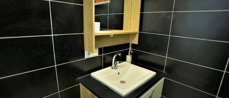 A bathroom with a white sink, black tiles, and a wooden cabinet above the sink.