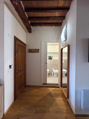 A hallway with a wooden door, a coat rack, and a mirror reflecting a bathroom with a toilet and bidet. - Lucca Luxury Historic Center Apartment (Lucca)
