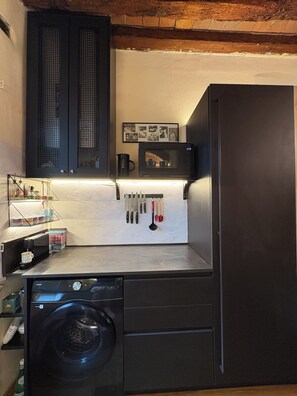 A compact kitchen with a washing machine, a microwave, and a refrigerator. - Lucca Luxury Historic Center Apartment (Lucca)
