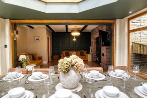 Ein Essbereich mit einem Tisch, der für sechs Personen gedeckt ist, einer großen Blumenvase und einem Kamin aus Backsteinen im Hintergrund.