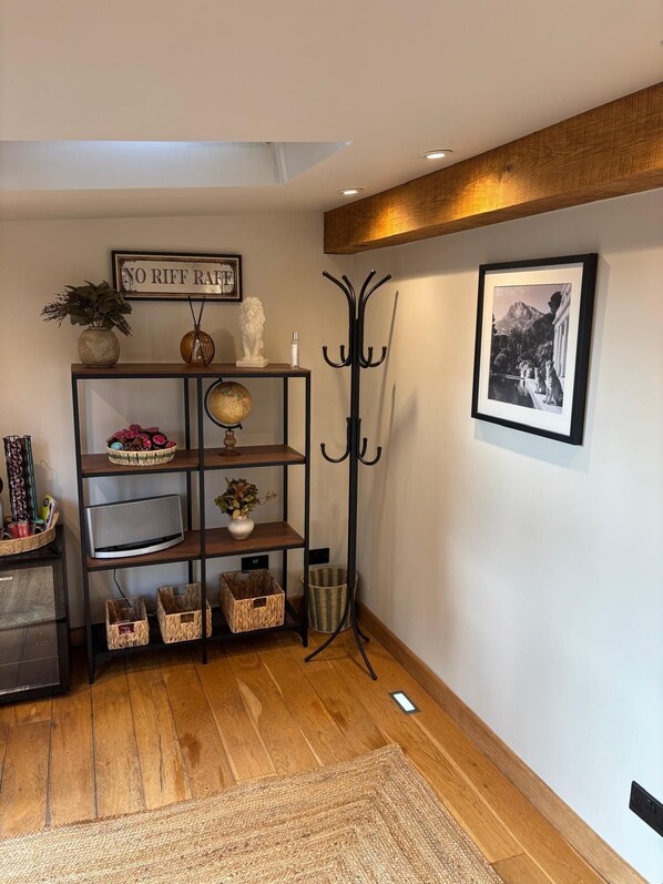A hallway with a wooden floor, a black coat rack, a framed sign, a globe, and a shelf with baskets and a sculpture. - Luxurious Spacious Countryside House | Big Jacuzzi & Gym (Bristol)