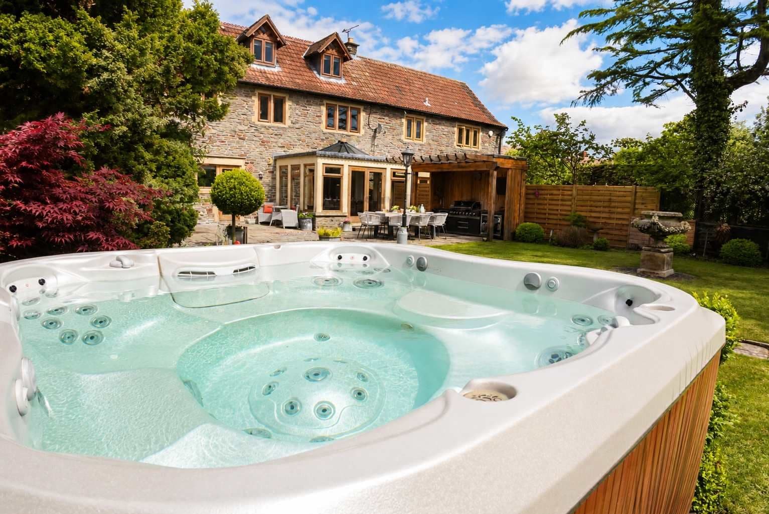 Ein Whirlpool in einem Garten mit einem Steinhaus im Hintergrund.