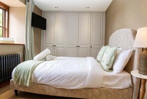 A neatly made bed with white linens and a green throw blanket, a bedside lamp, and a window with curtains. - Luxurious Spacious Countryside House | Big Jacuzzi & Gym (Bristol)