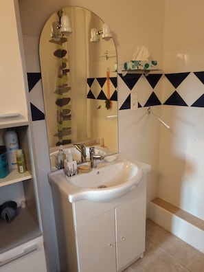 A bathroom with a white sink, a mirror, and a towel rack. There are toiletries on the shelf and a shower curtain with a geometric pattern. - Studio in the countryside with a view of the Pyrenees. (Castillon-de-Saint-Martory)