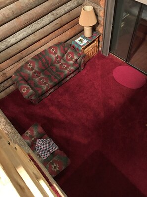 Ein gemütliches Zimmer mit einer gemusterten Couch, einem kleinen Tisch mit einer Lampe und einem roten Teppich.