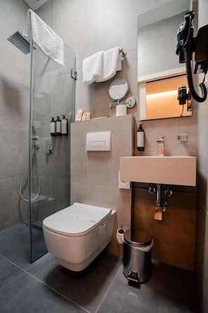 A modern bathroom with a glass shower enclosure, a toilet, a sink with a mirror, and a trash bin. - Casa Versus Ohrid (ohrid)