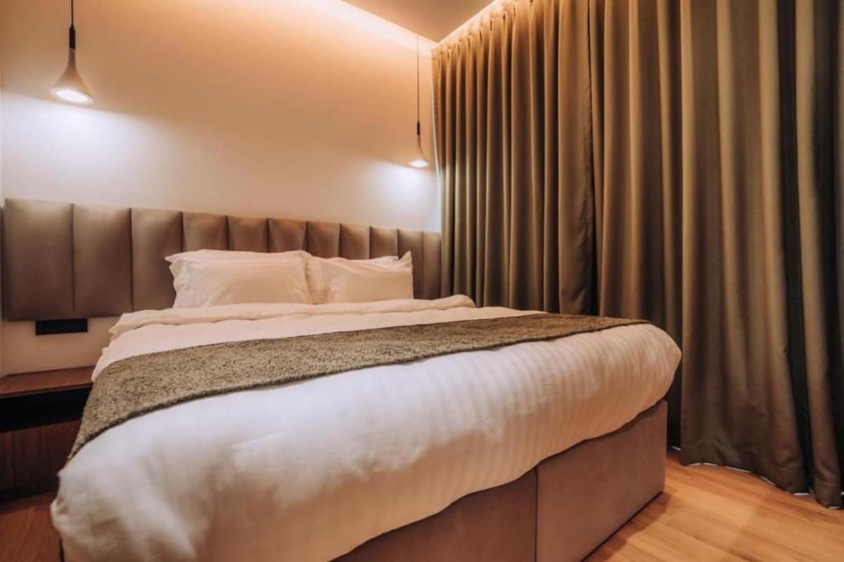 A bedroom with a large bed, a headboard, a bedside table, and a curtain.