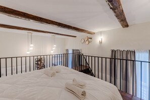 Ein Schlafzimmer mit einem großen Bett, einem Holzbalken, einem schwarzen Geländer und einer Treppe.