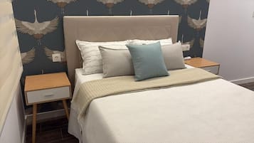 Una cama bien hecha con cabecera, dos mesitas de noche y una pared con un motivo de pájaros.
