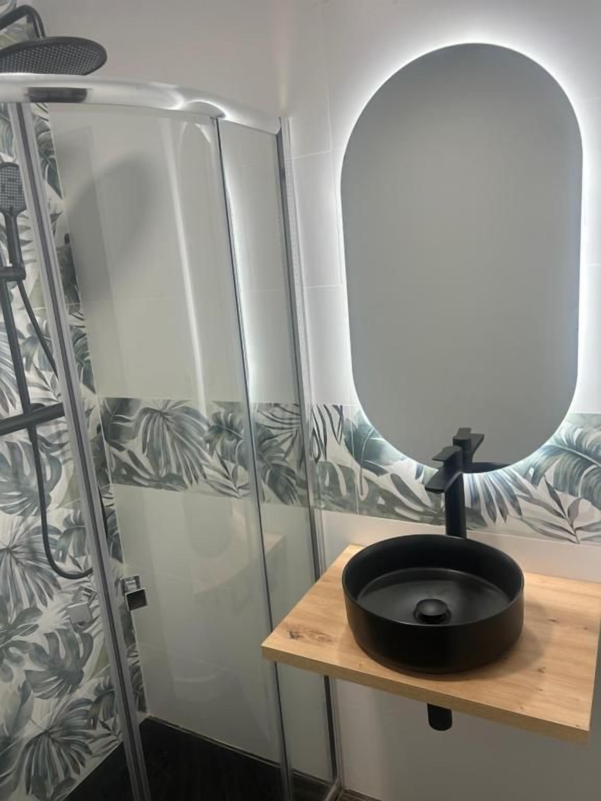 Un baño con cabina de ducha, espejo y lavamanos con estante de madera.
