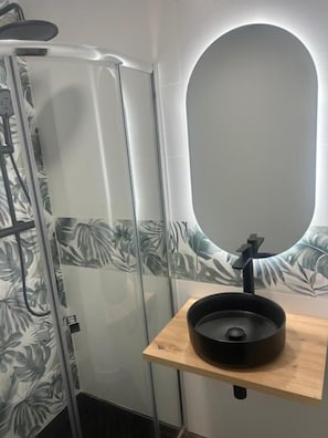 Ein Badezimmer mit Duschkabine, Spiegel und Waschbecken mit Holzablage.