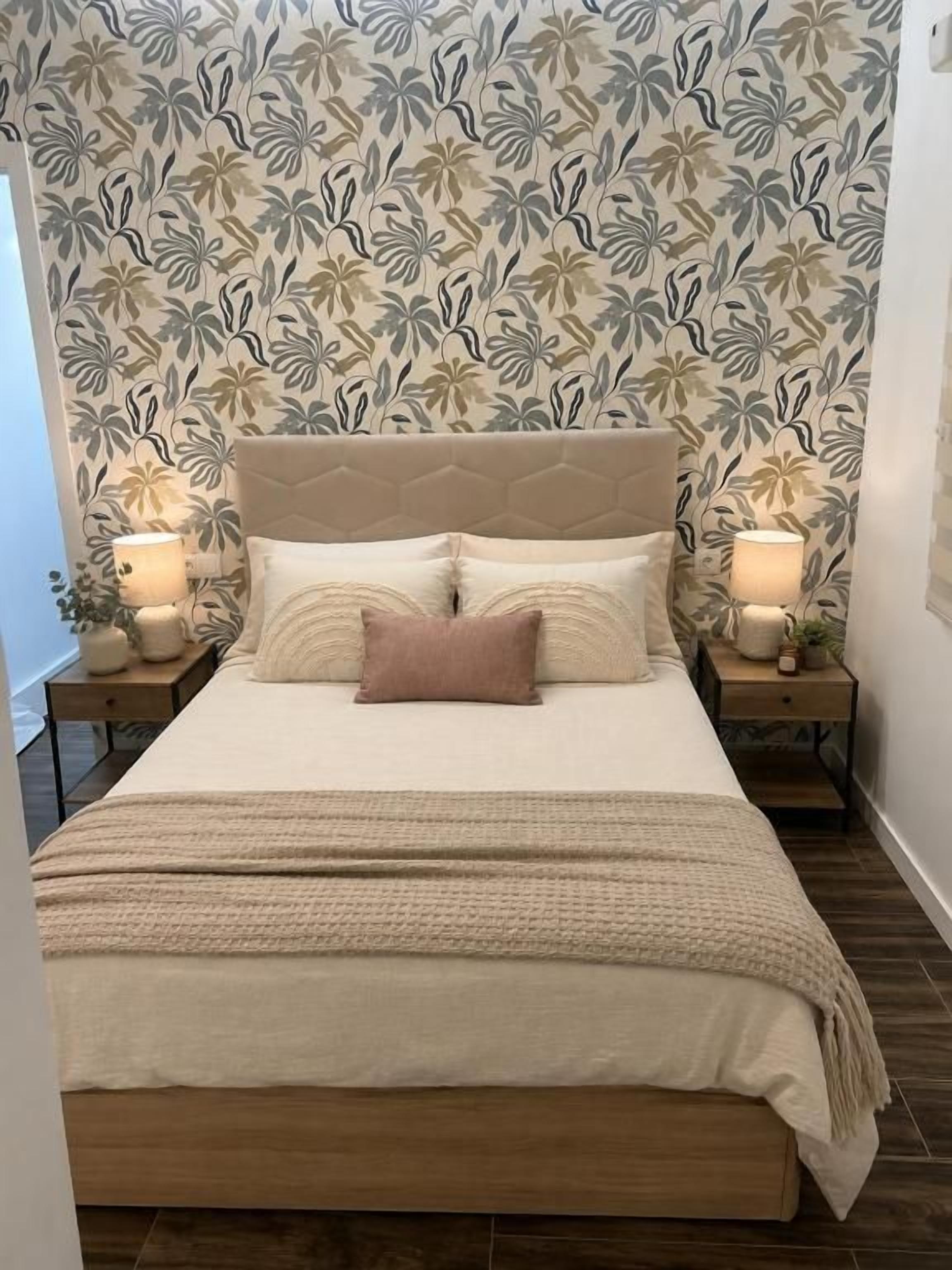 Un dormitorio con cama, mesitas de noche y un papel tapiz estampado.