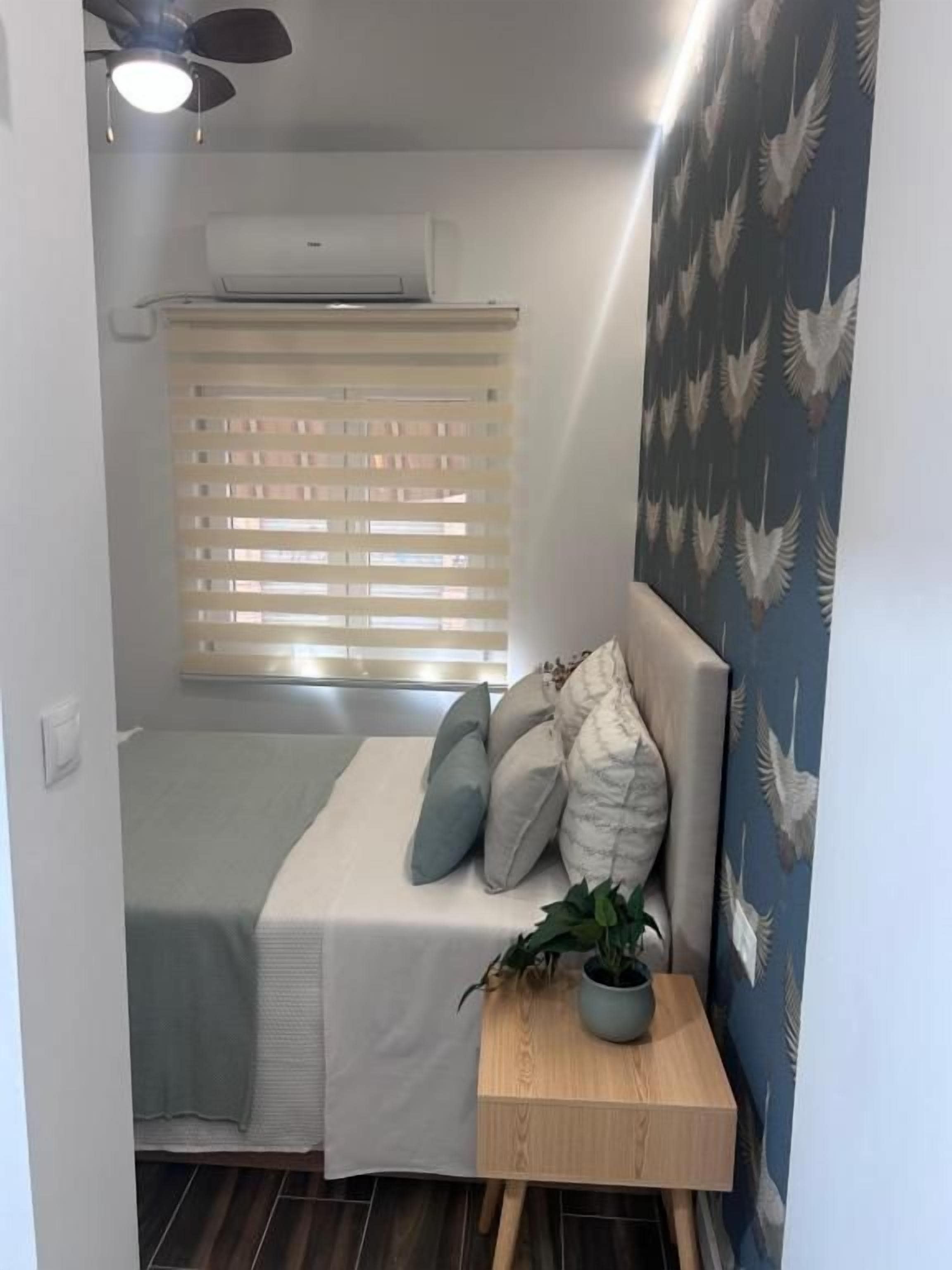 Una habitación pequeña y acogedora con cama, una mesita de noche con una planta y una ventana con persianas.
