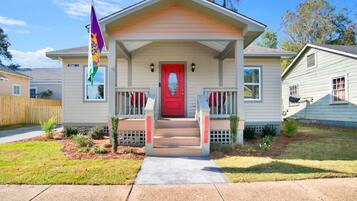 A single-story house with a red front door, a porch with steps, and a flagpole with a flag.