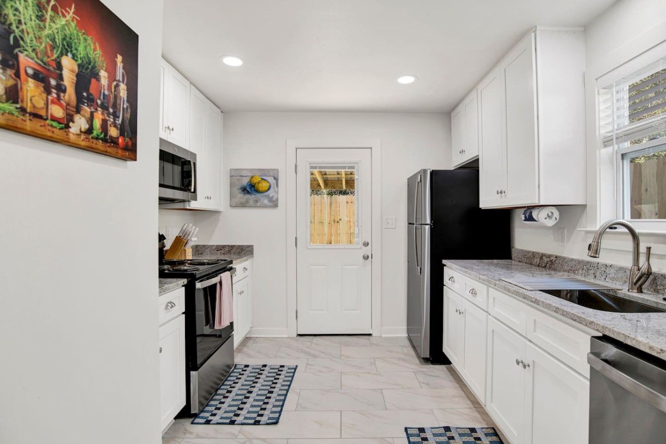 A compact kitchen with white cabinets, a stainless steel refrigerator, a microwave, and a sink.