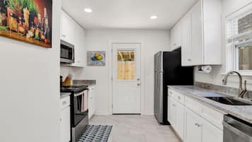 A compact kitchen with white cabinets, a stainless steel refrigerator, a microwave, and a sink.