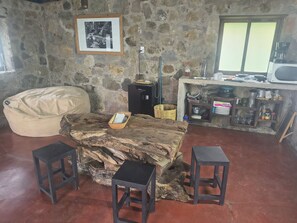 A rustic interior with a stone wall, a framed photograph, a wooden table with stools, and a kitchenette area. - Cabaña Tetitla — Una escapada entre naturaleza y tradición en Tlaxcala. (Amaxac de Guerrero)