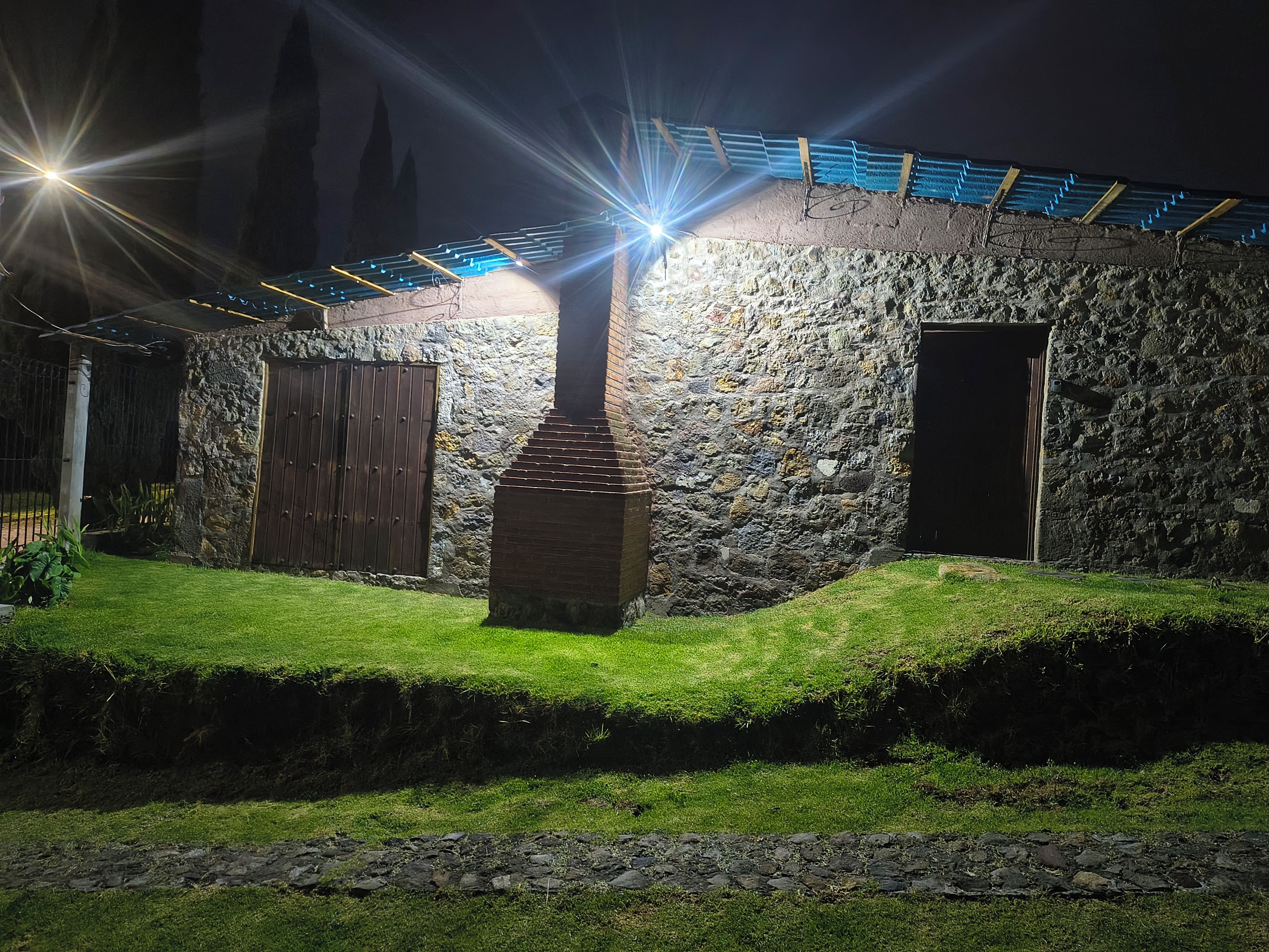 A stone building with a central chimney, a wooden door, and a metal roof.