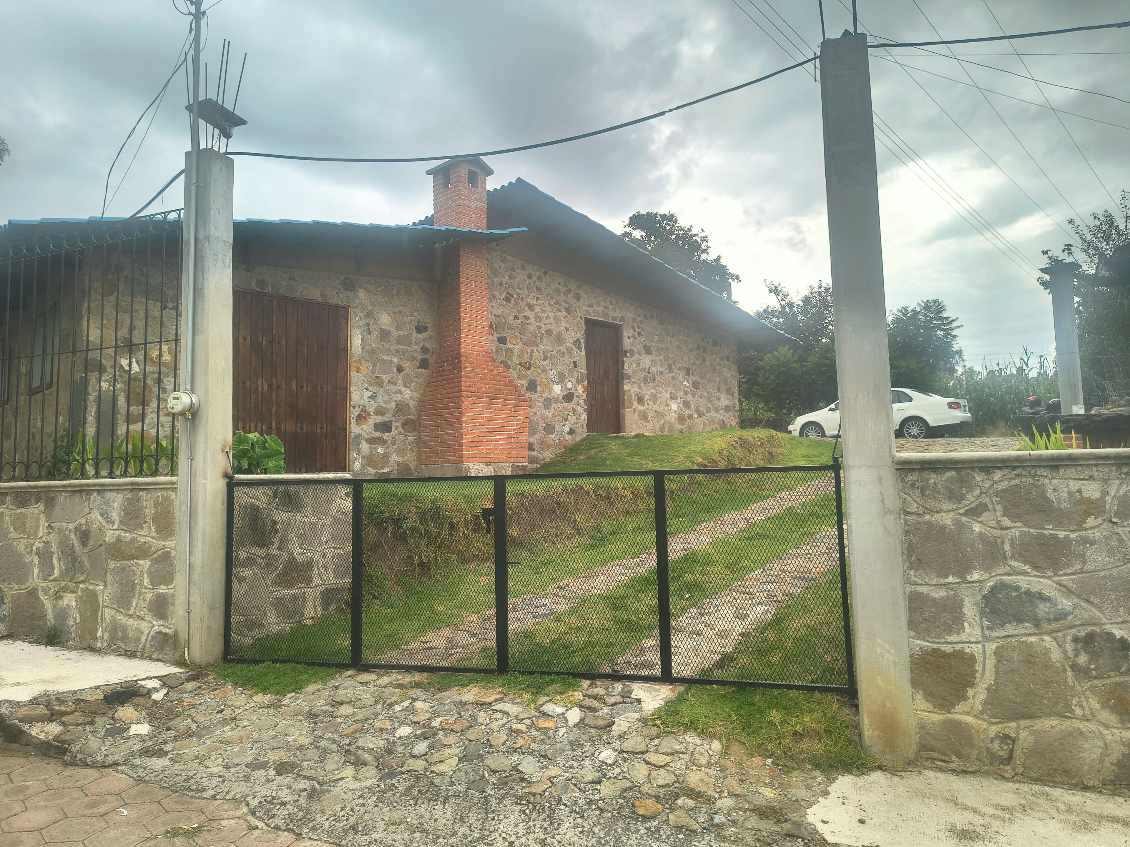 Un edificio de piedra con una chimenea de ladrillo, una reja de metal y un coche blanco estacionado cerca.