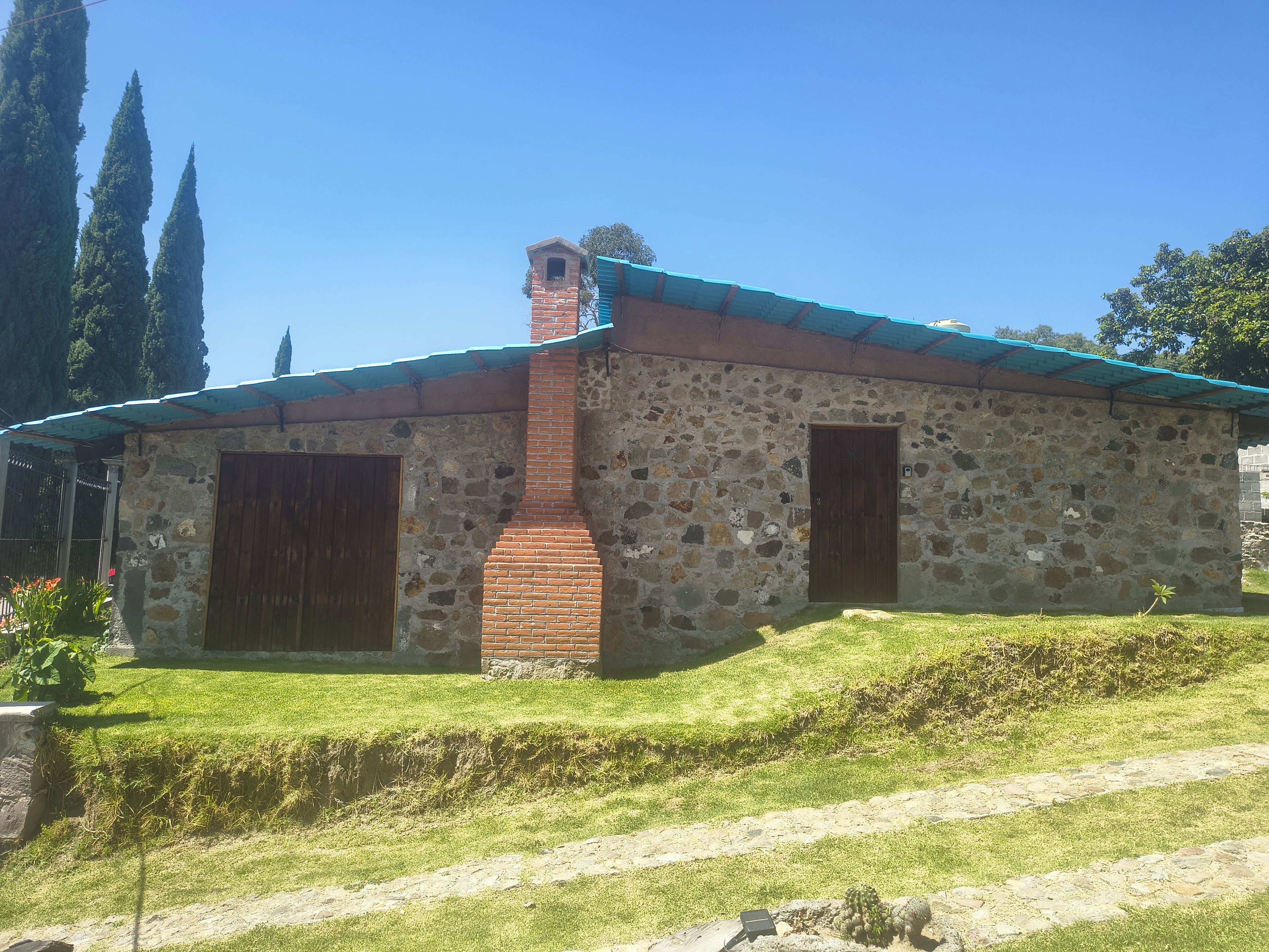 Un bâtiment en pierre avec une cheminée en briques, deux portes en bois et un toit en métal.