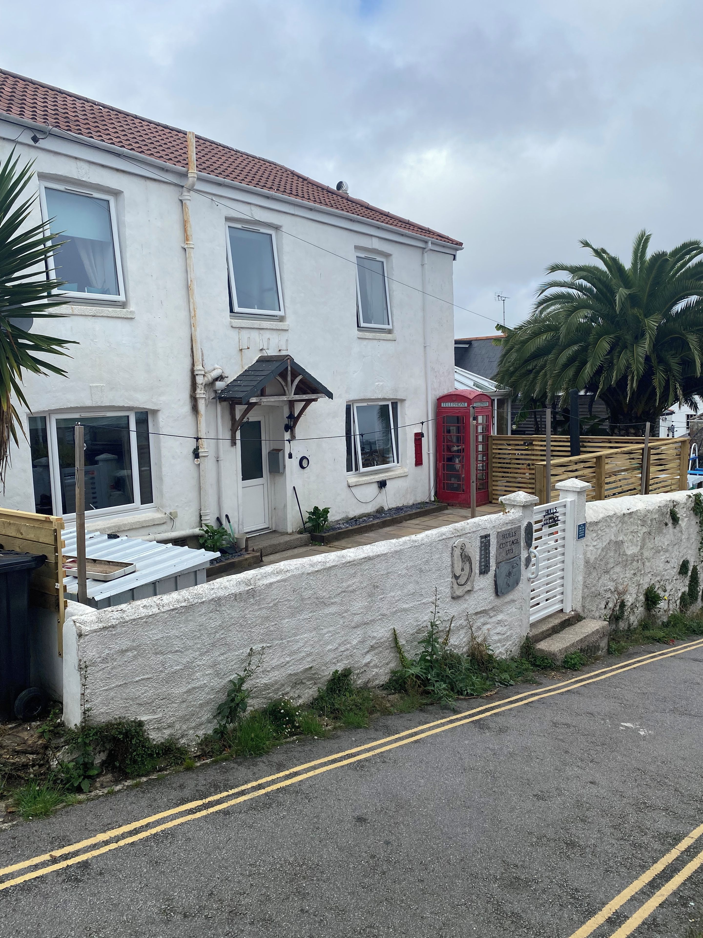 A two-story building with a red telephone booth, a white wall with a plaque, and a paved road with double yellow lines.