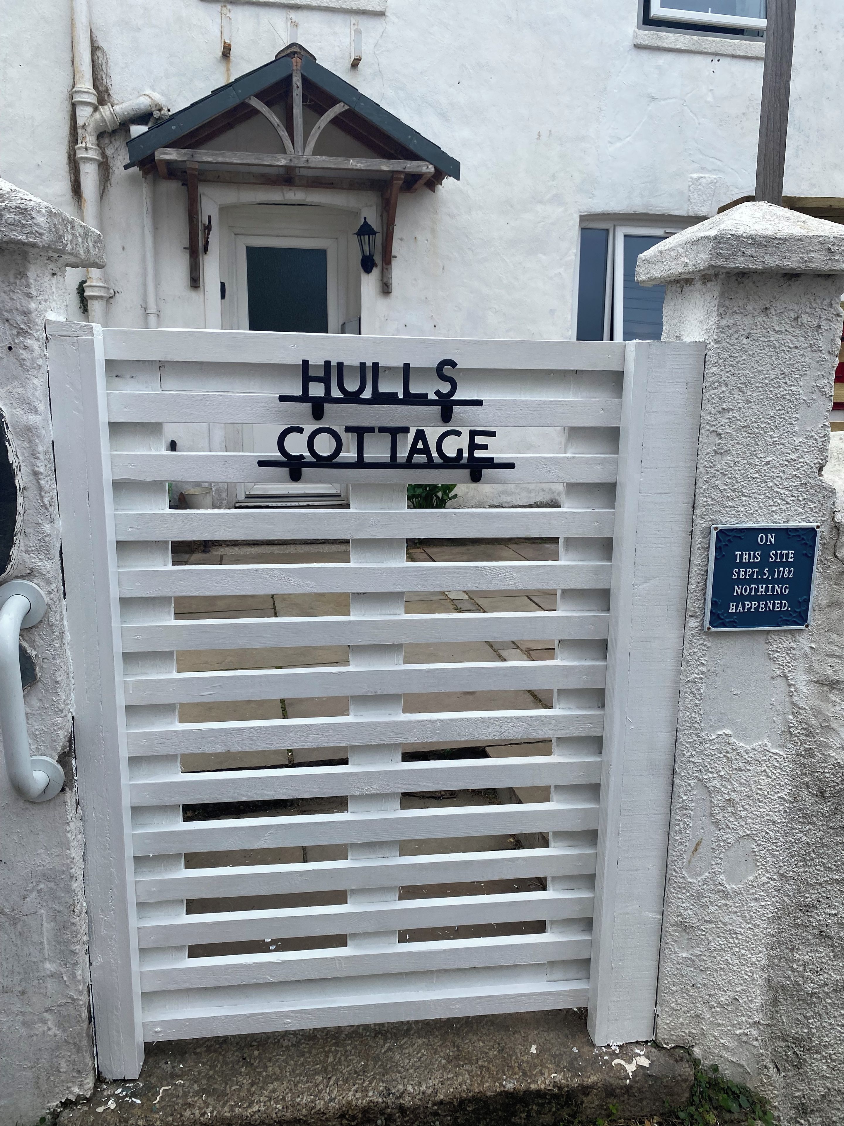Une entrée fermée par un portail mène à la maison de campagne de Hulls, avec une enseigne au-dessus du portail et une plaque fixée au mur.