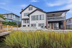 A two-story house with a balcony, a deck, and a pond with tall grass. - Marsh Bend: 8  BR, 5  BA House in Pawleys Island, Sleeps 21 (Pawleys Island)