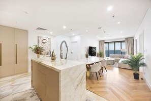 A modern living space with a marble island, a dining area, a sofa, and a large window offering a view. - Upgraded 2BR Anantara Burj & Sea View (Dubai)