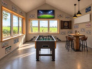 A room with a foosball table, a dartboard, and a TV mounted on the wall. - Schmiede I - Vacation Home for 8 People with 4 Bedrooms & a Garden (Dagebüll)