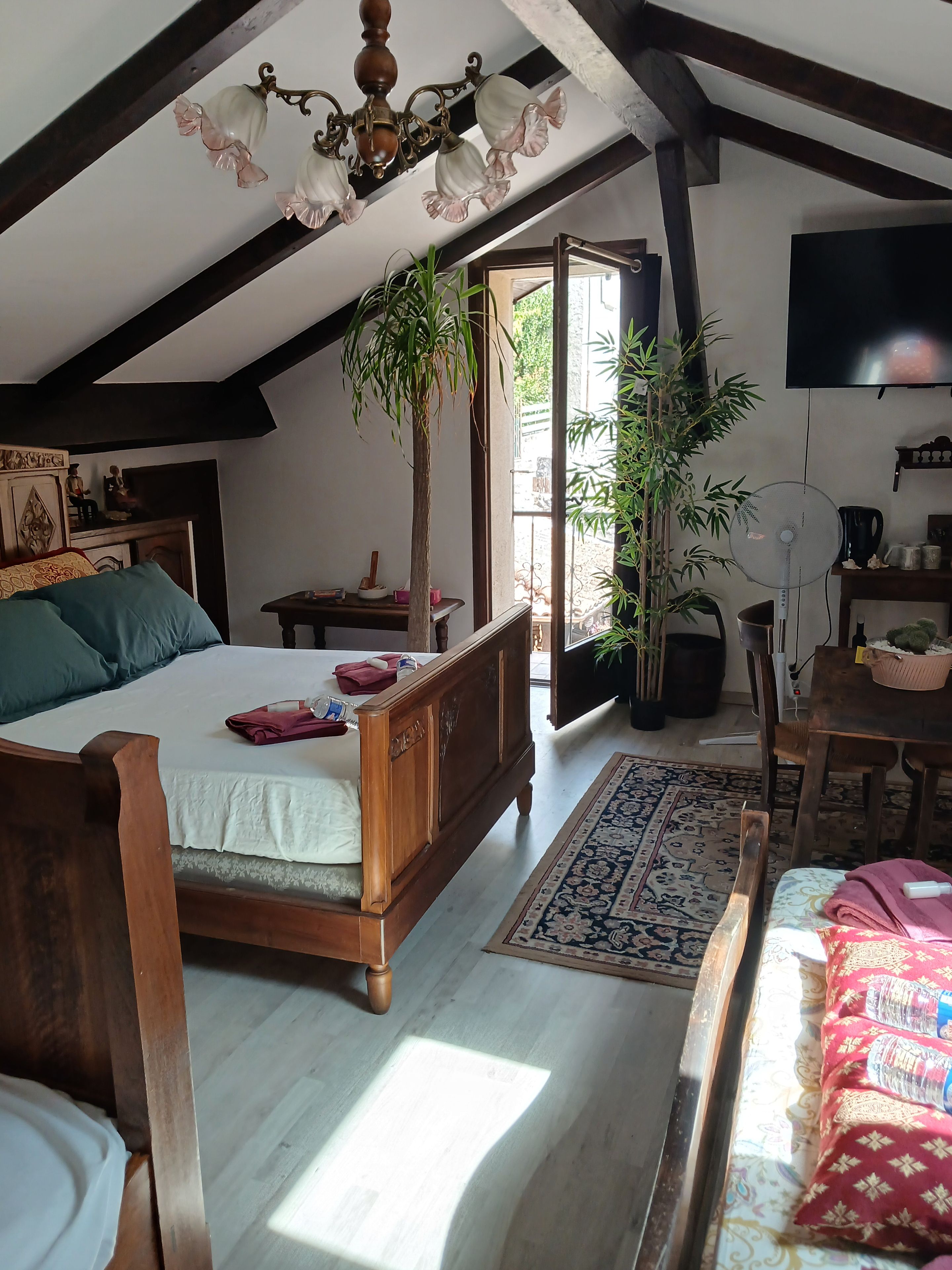 Une chambre avec un lit en bois, un ventilateur de plafond et une grande fenêtre.