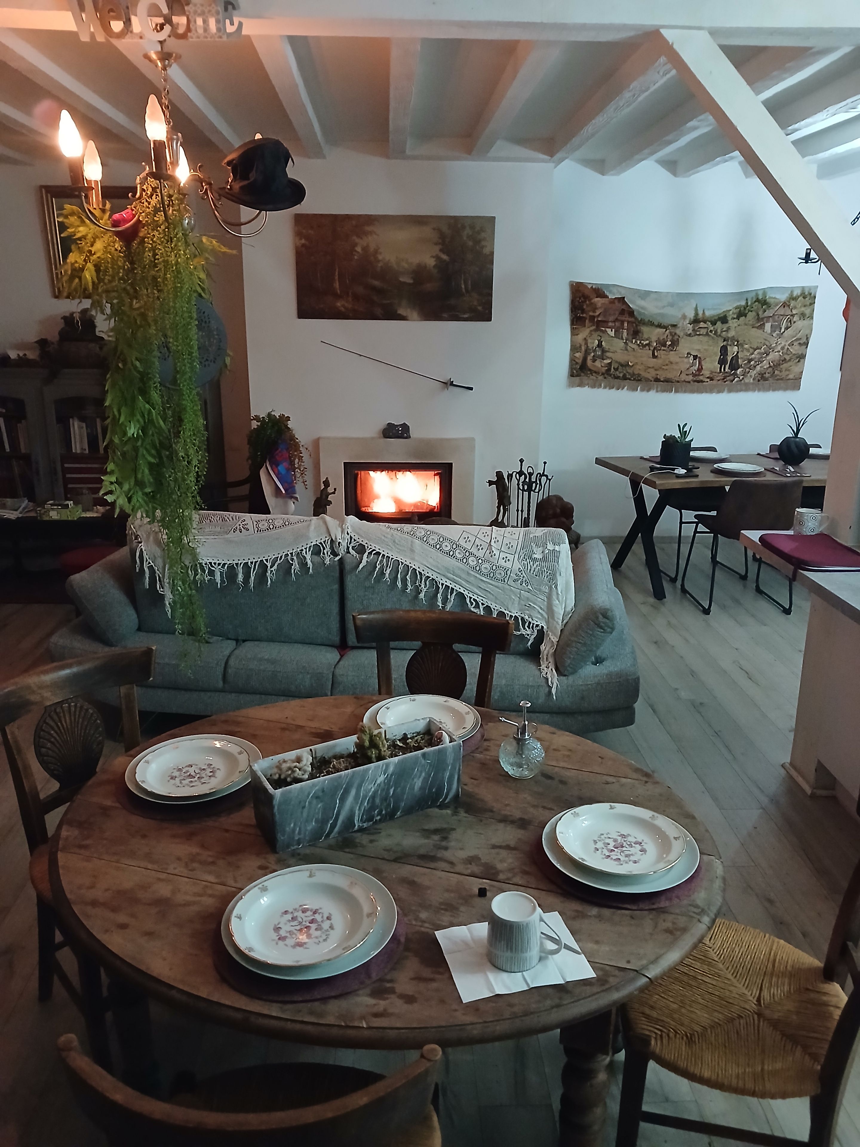 Un accogliente soggiorno con camino, un tavolo da pranzo apparecchiato con piatti e una ciotola, e un divano con una coperta.
