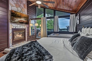 A bedroom with a fireplace, a large bed, a view of the outdoors, and a ceiling fan. - Intimate Couples Oasis! Views! Movie Theater! Love (Pigeon Forge)