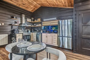 A modern kitchen with dark wood paneling, stainless steel appliances, and a dining area with a round table and chairs. - Intimate Couples Oasis! Views! Movie Theater! Love (Pigeon Forge)
