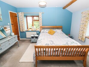Ein Schlafzimmer mit einem hölzernen Bett, einem Schminktisch, einem Nachttisch, einem Fenster mit Vorhängen und einer Heizung.