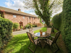 A stone building with a grassy yard, a round table with chairs, and a wooden gate. - Greig House Cottage (Abergavenny)