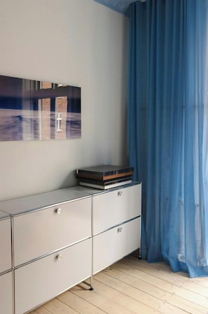 Une pièce avec une commode blanche, un tableau encadré au mur et un rideau bleu.