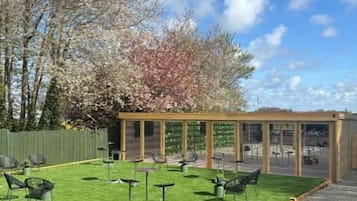 Un espace patio avec des sièges d’extérieur, une pergola et une vue sur les arbres et le ciel.